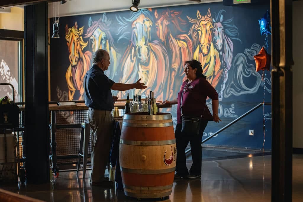 Two members talking beside the painted-horses mural at a community event.