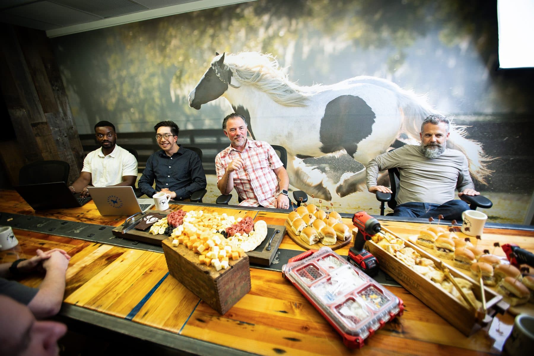 Members talking around a table spread with food, beneath a large photograph of horses.