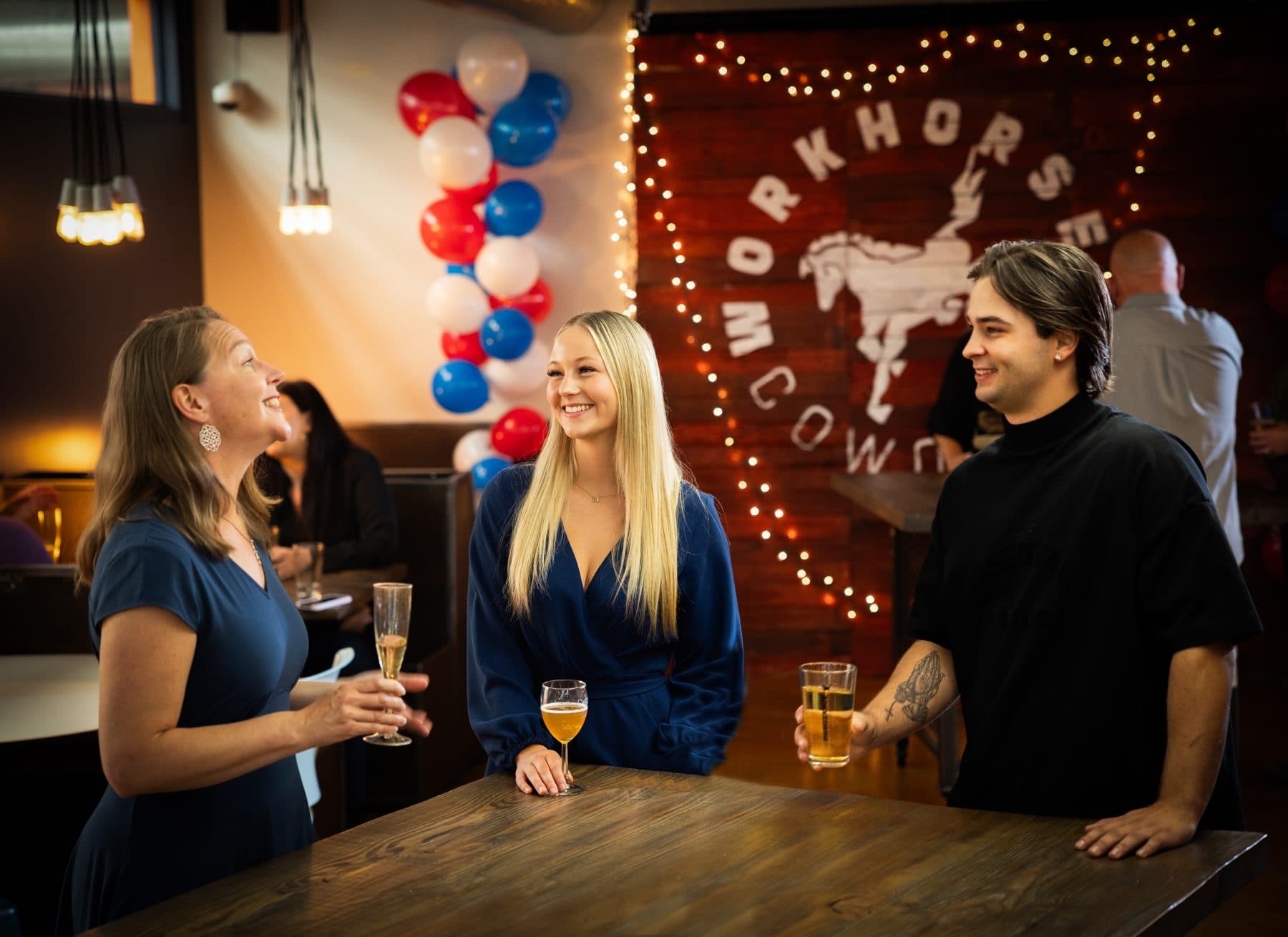 Members talking with drinks in hand beneath the lit Workhorse Coworking sign.