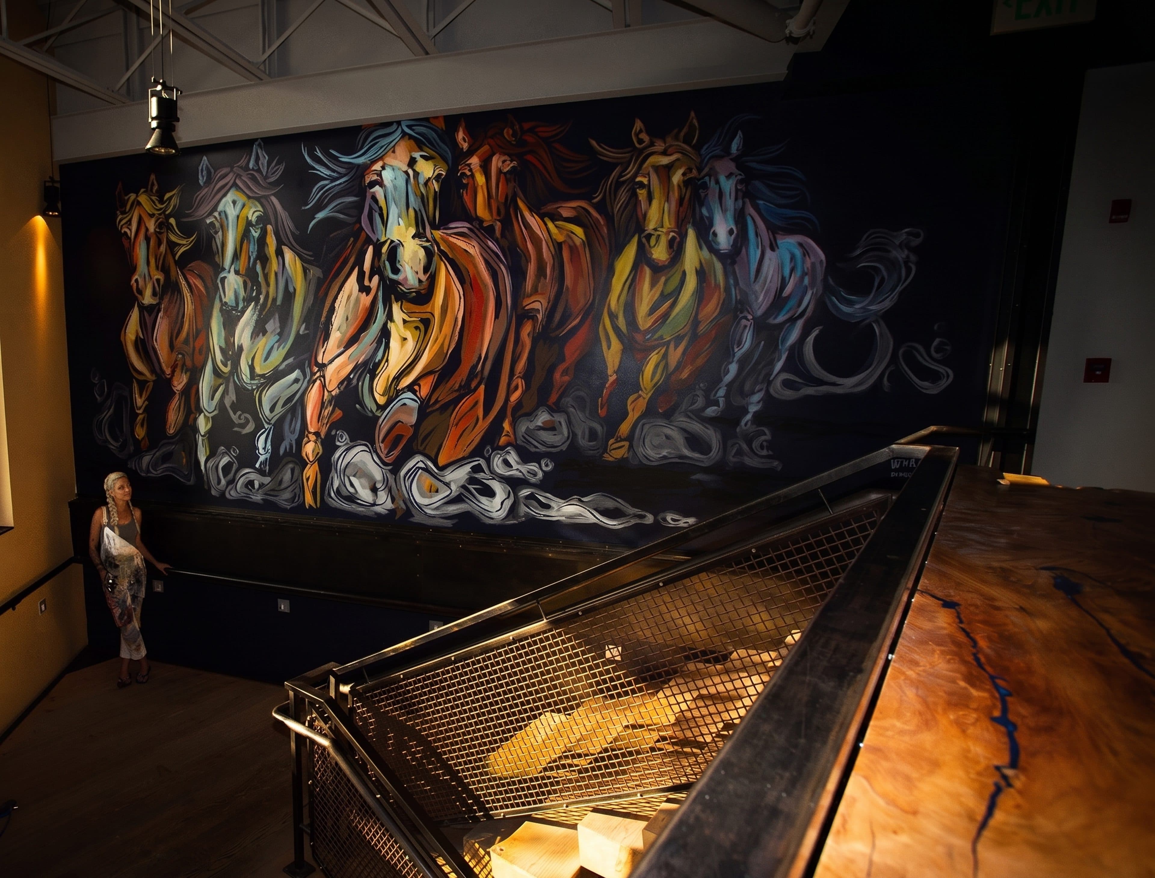 The galloping-horses mural seen from above the live-edge bar, the artist standing at the far left for scale.