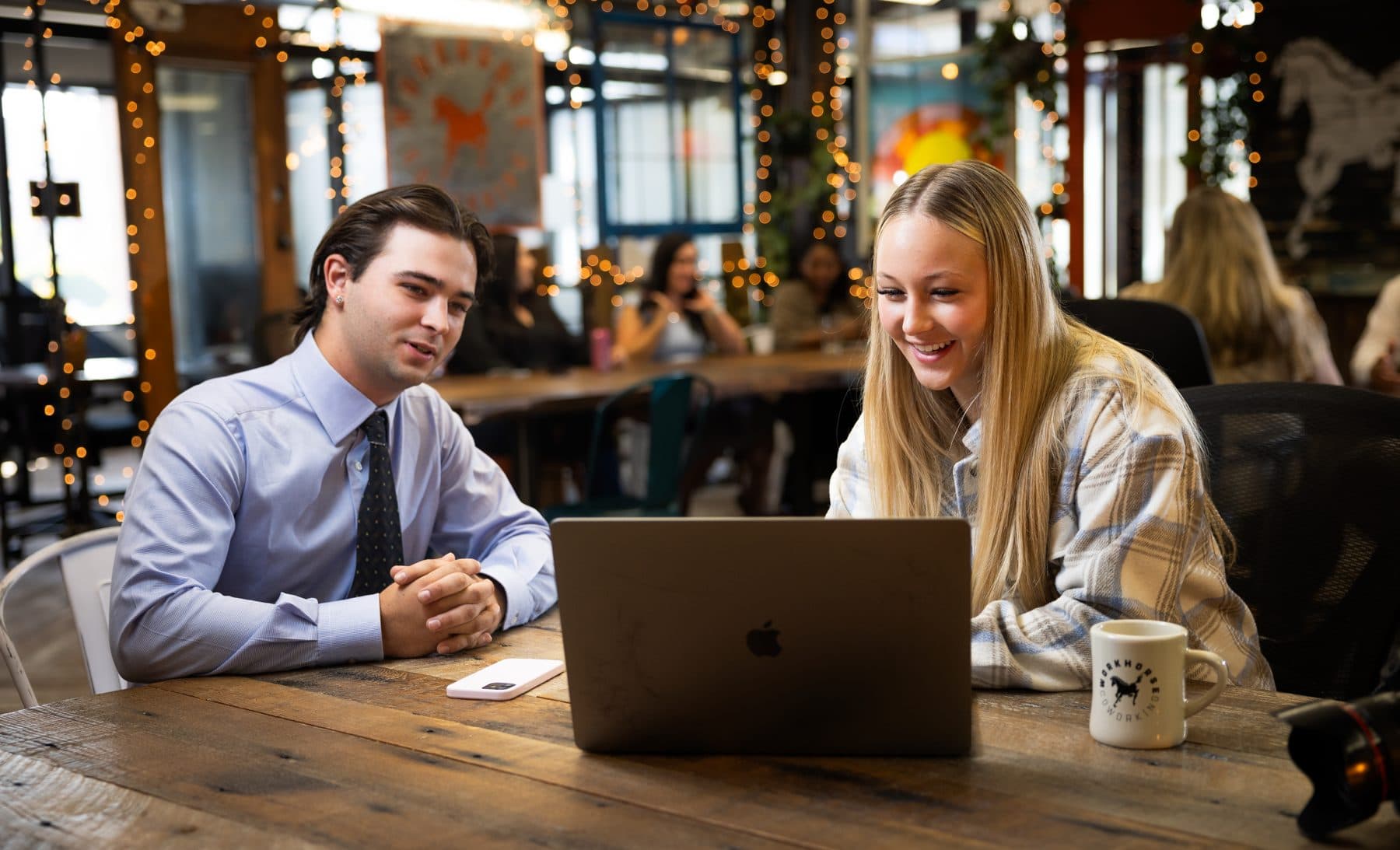 Two members leaning in over a laptop together at the long wood table.