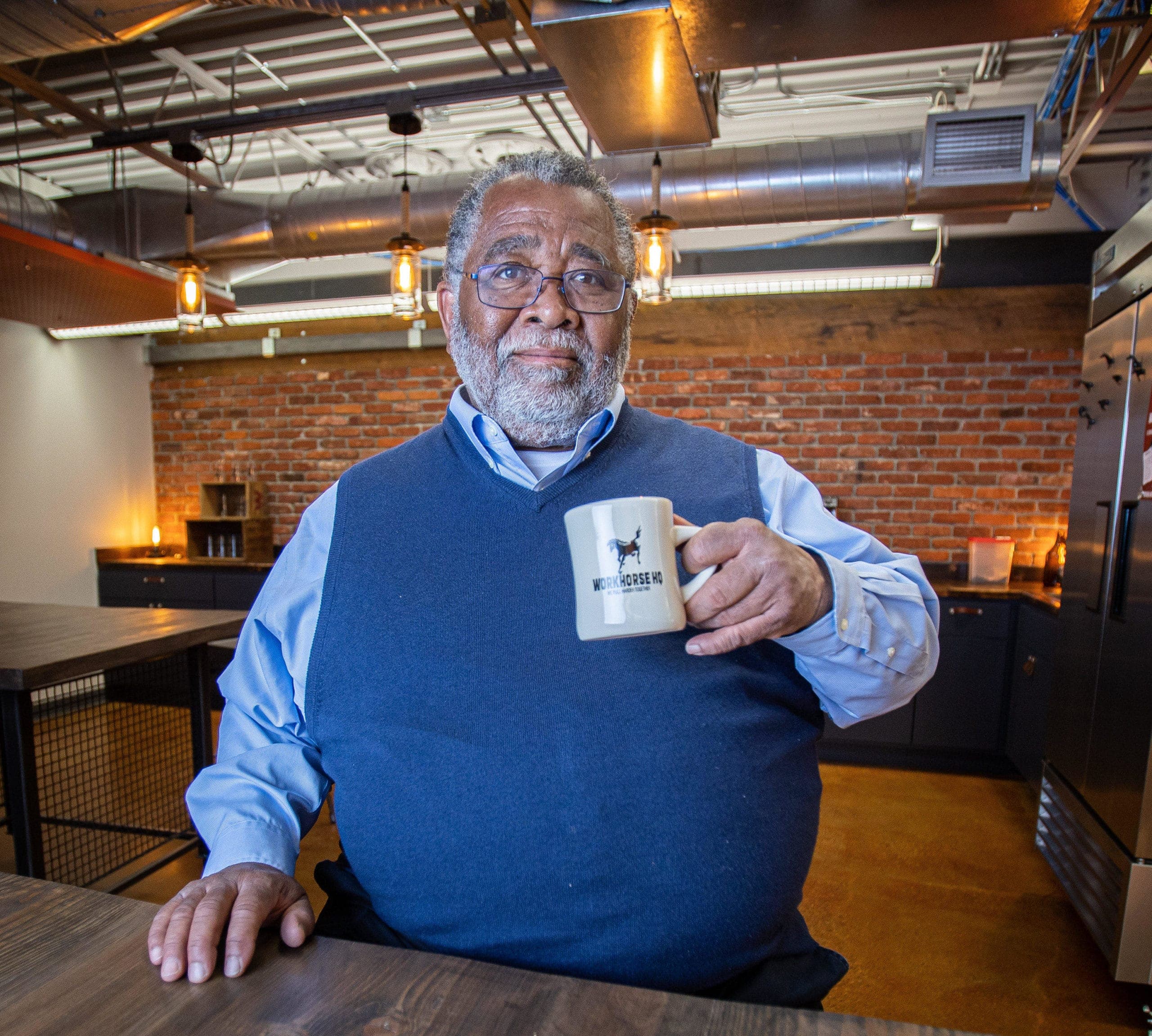 A member with a Workhorse mug in the kitchen, brick wall behind.