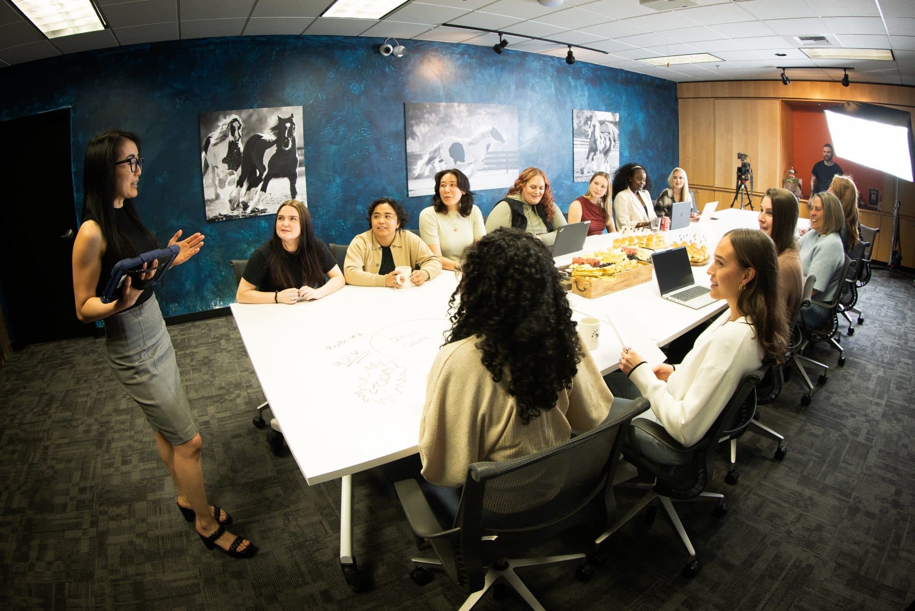 A full meeting around the long white boardroom table, framed horse photographs on the blue wall behind.