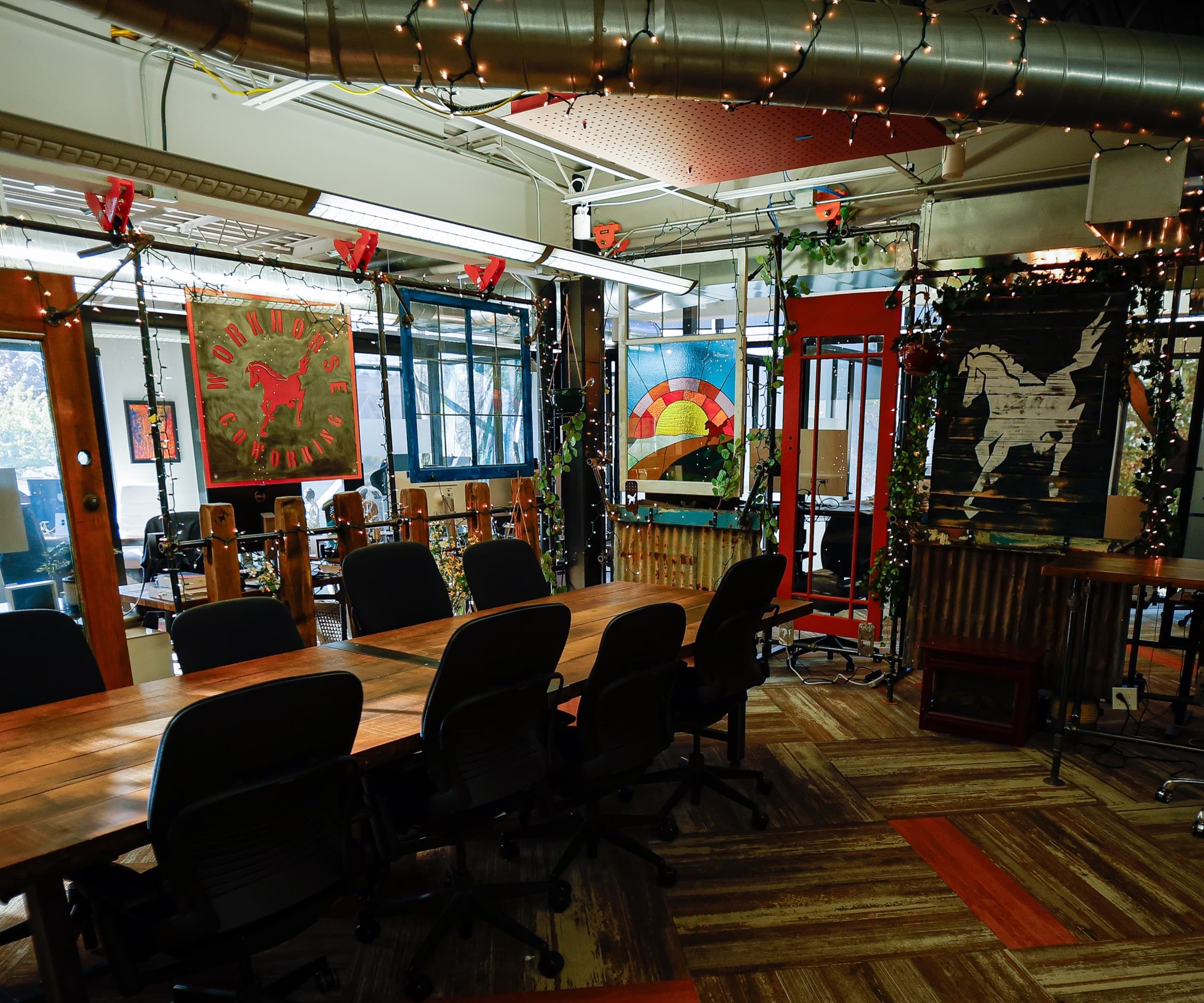 The main floor: a long reclaimed-wood table under string lights, the red Workhorse banner on one wall and a white horse painted on dark board on the other.