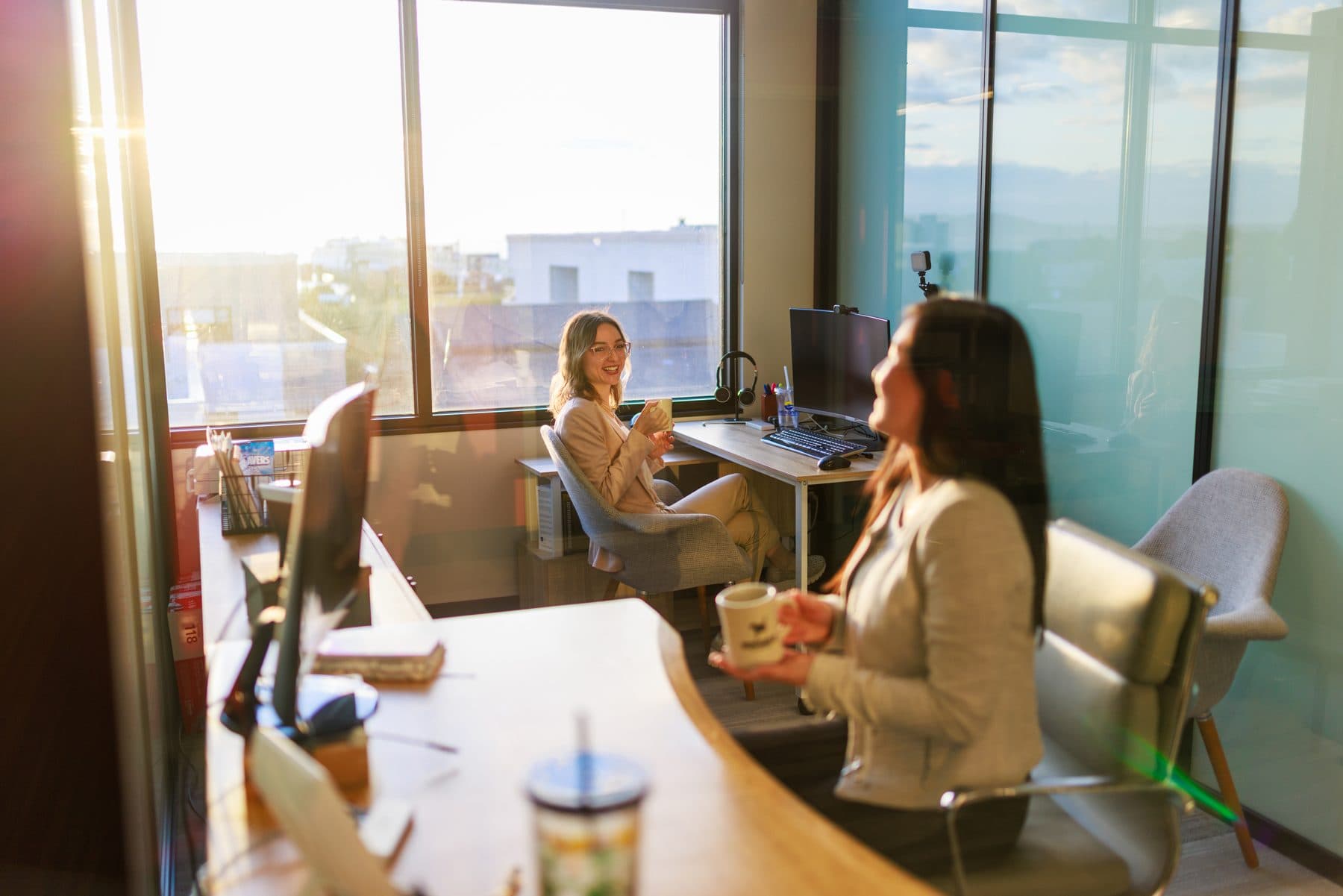 Two members talking across a desk in a private office as low evening sun comes through the windows.