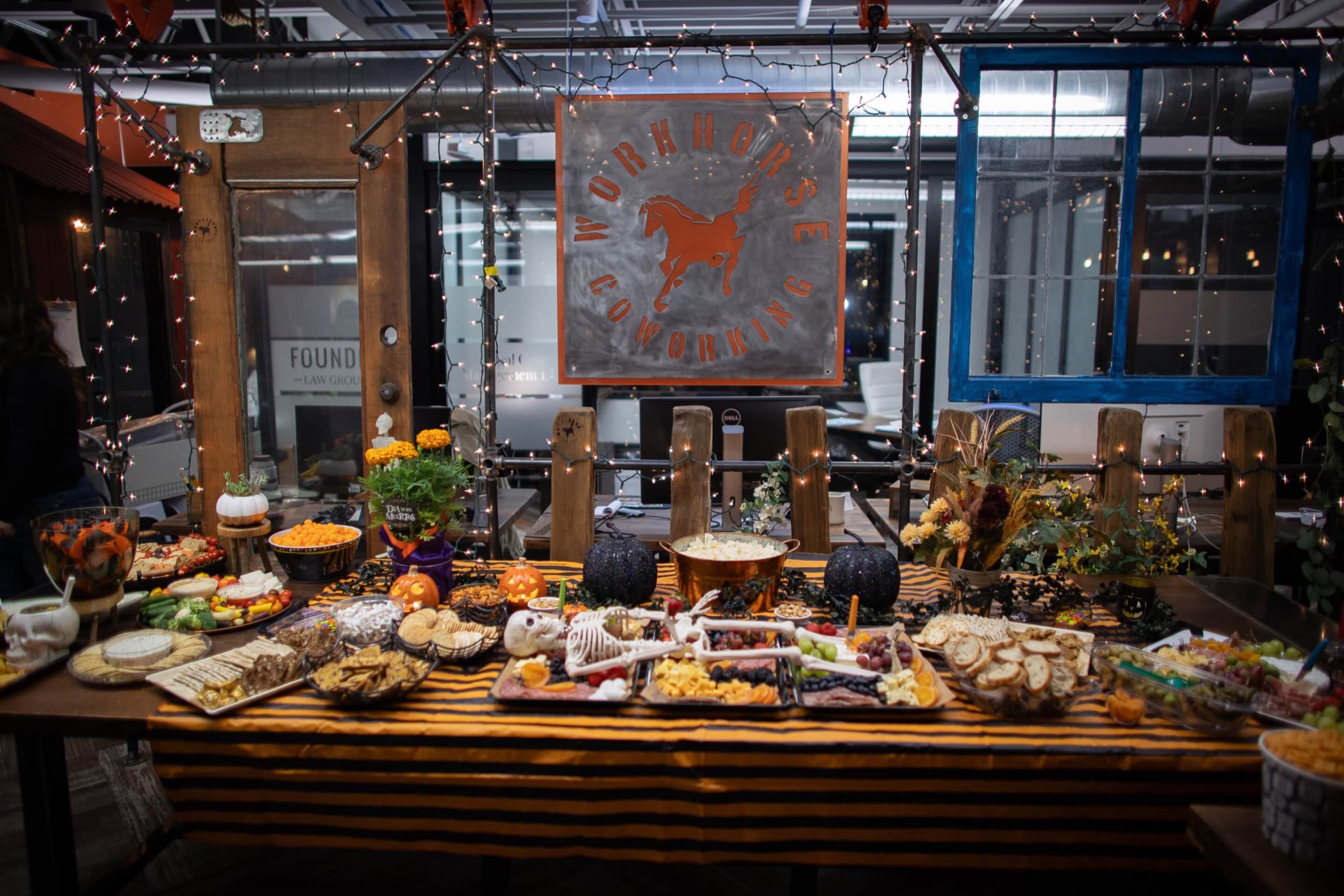The venue set for an event — a harvest table loaded with food beside the glass wall.