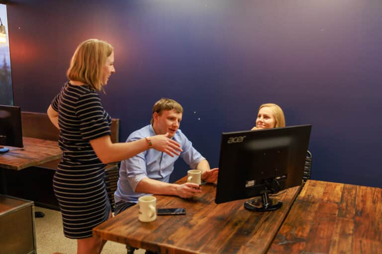 Three workers collaborating around a monitor
